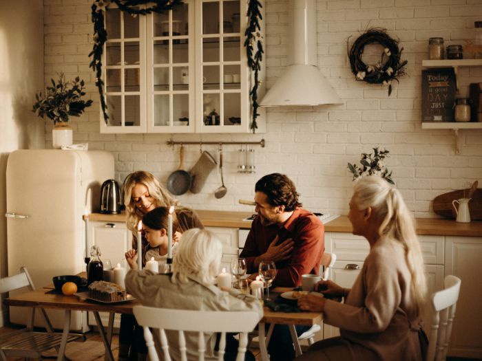 Eine fünfköpfige Familie sitzt an einem Tisch in einer mit weißen Möbeln im Landhausstil eingerichteten Küche.