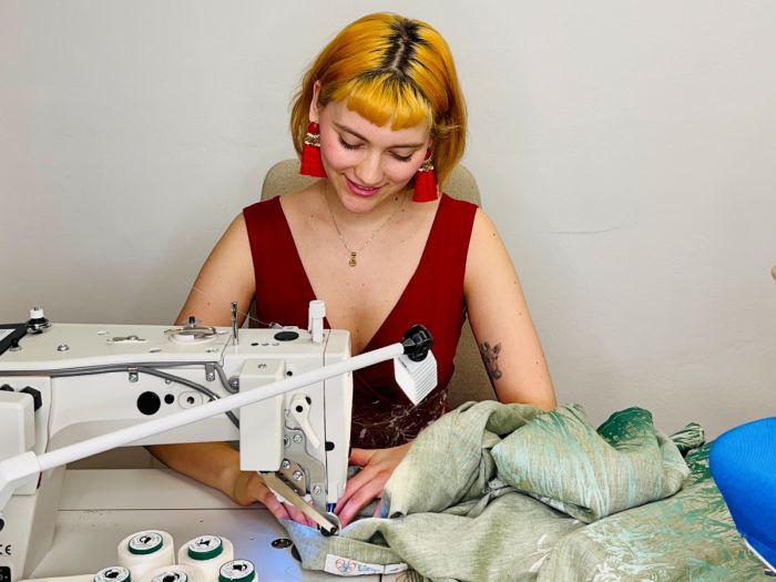 Eine junge Frau sitzt an einer Nähmaschine und fertigt einen Rock.