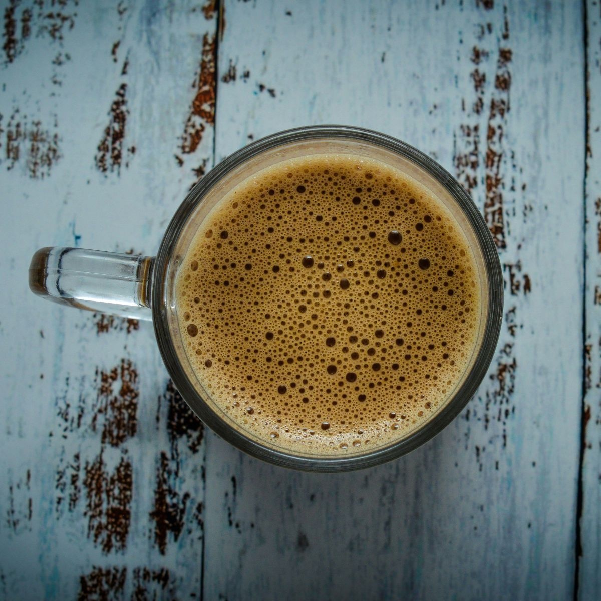 Ein Glas schäumender Kaffee von oben fotografiert, auf einer im shabby-chic-style Türkisblau lackierten Tischplatte.