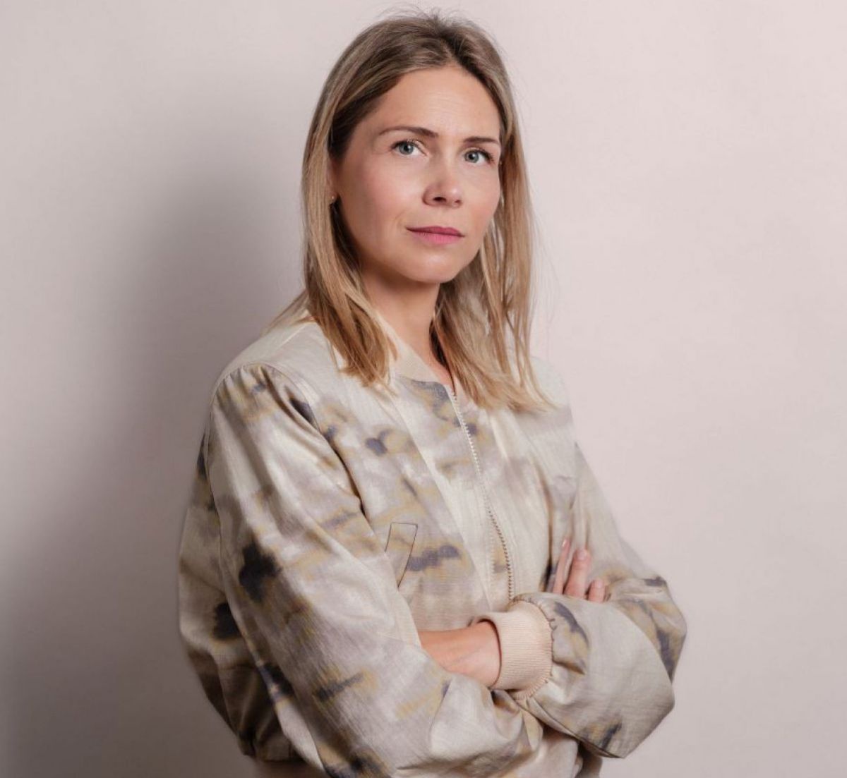 Eine Frau mit schulterlangen blonden Haaren blickt selbstbewusst in die Kamera.