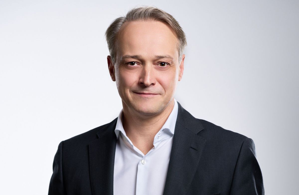 Ein Mann mit kurzen Haaren, weißem Hemd und schwarzem Sakko blickt leicht lächelnd in die Kamera.