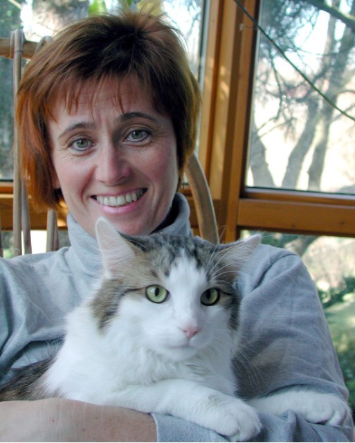 Eine Frau mit roten Haaren hält eine weiß-grau-gemusterte Katze am Schoß und lächelt in die Kamera.