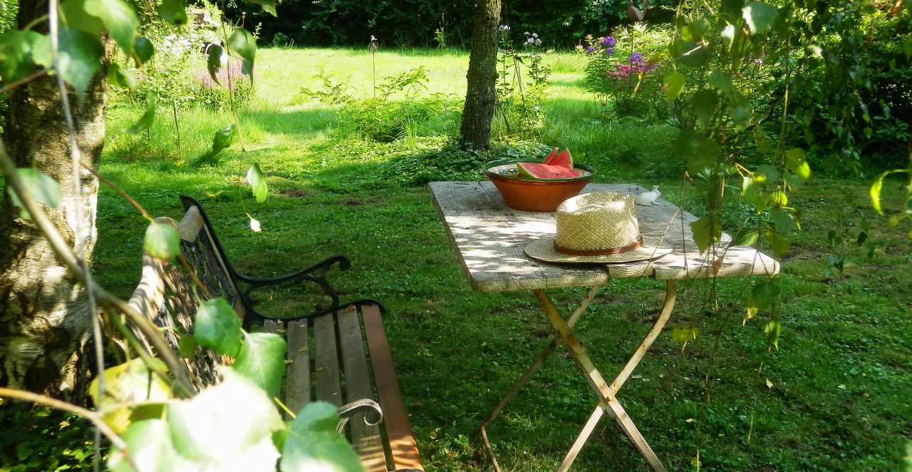In einem Garten steht auf einem Klapptisch eine Schüssel Wassermelonen, daneben ein liegt ein Strohhut.