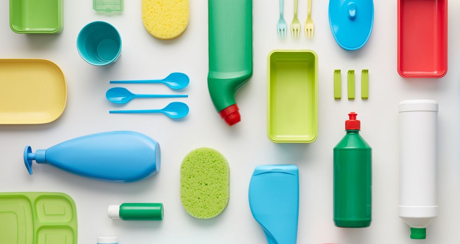 Auf einem weißen Hintergrund sind bunte Schwämme, Plastikflaschen und Plastikbesteck aufgelegt.