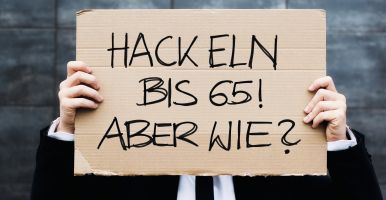 Eine Person mit Anzug und Krawatte hält ein Pappschild vor das Gesicht. Darauf steht 