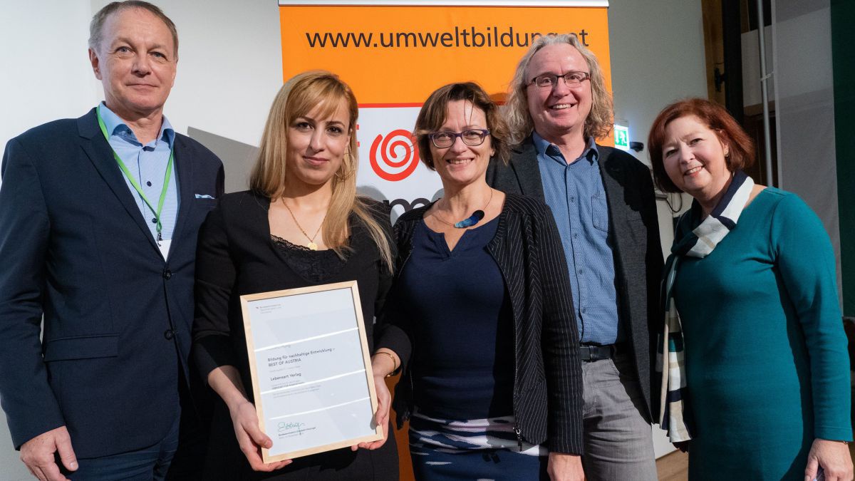 Fünf Personen stehen zusammen, eine davon hält eine Urkunde in H#änden. Dahinter das Banner von Umweltbildung.