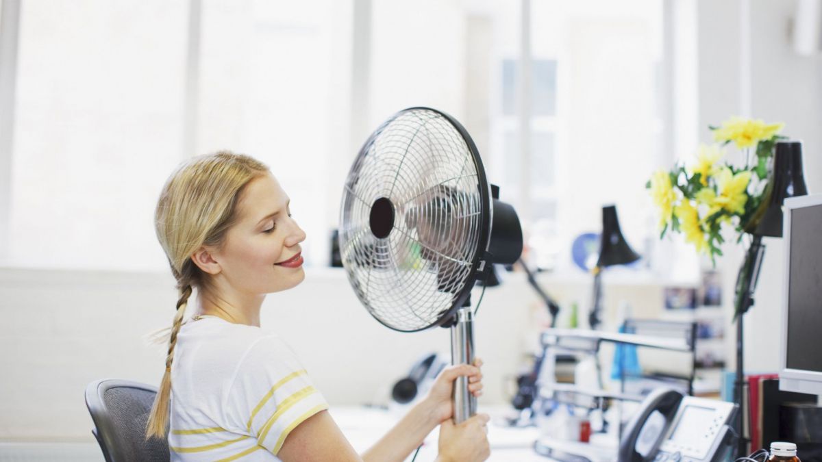 Frau sitzt vor Ventilator im Büro.