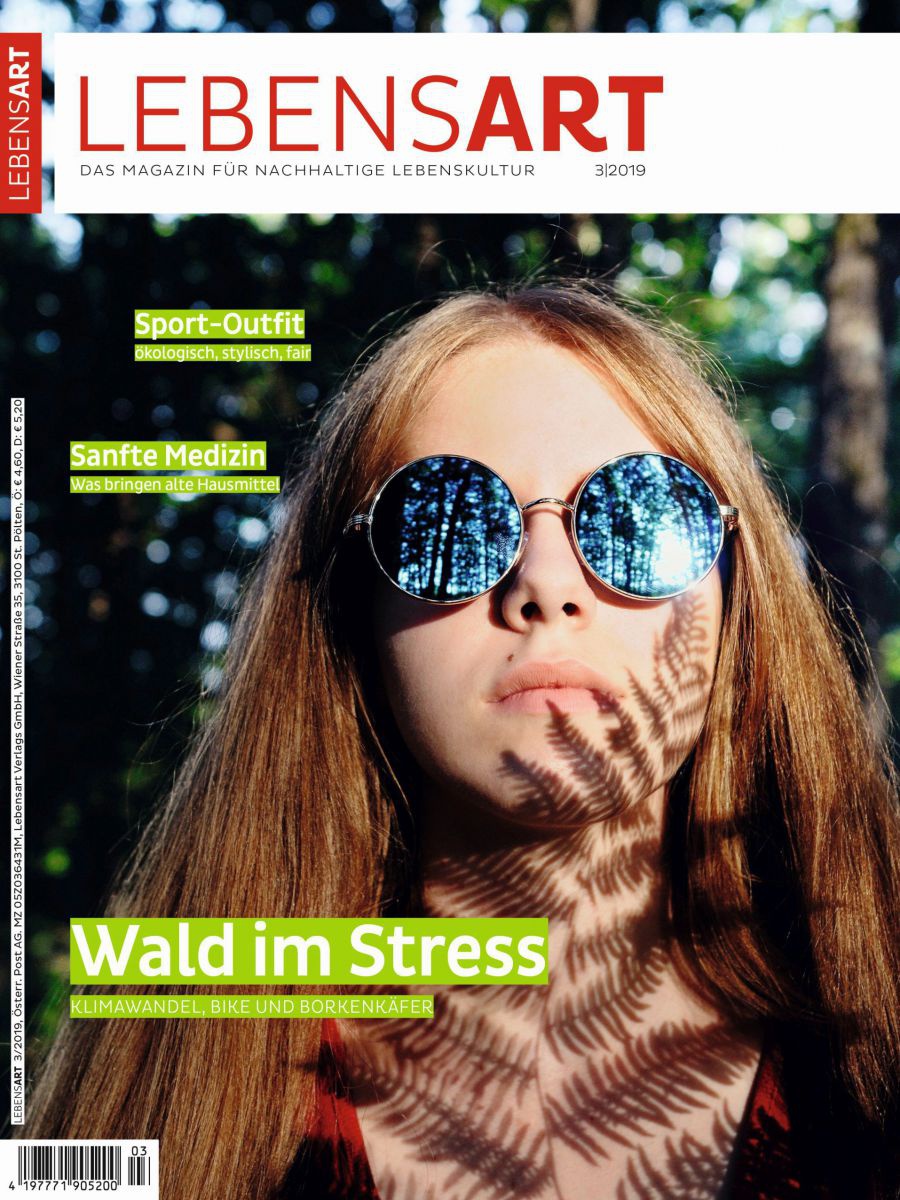 Das Gesicht einer jungen Frau. Ein Farn wirft Schatten darauf, in den Gläsern ihrer Sonnenbrille spiegeln sich Bäume.