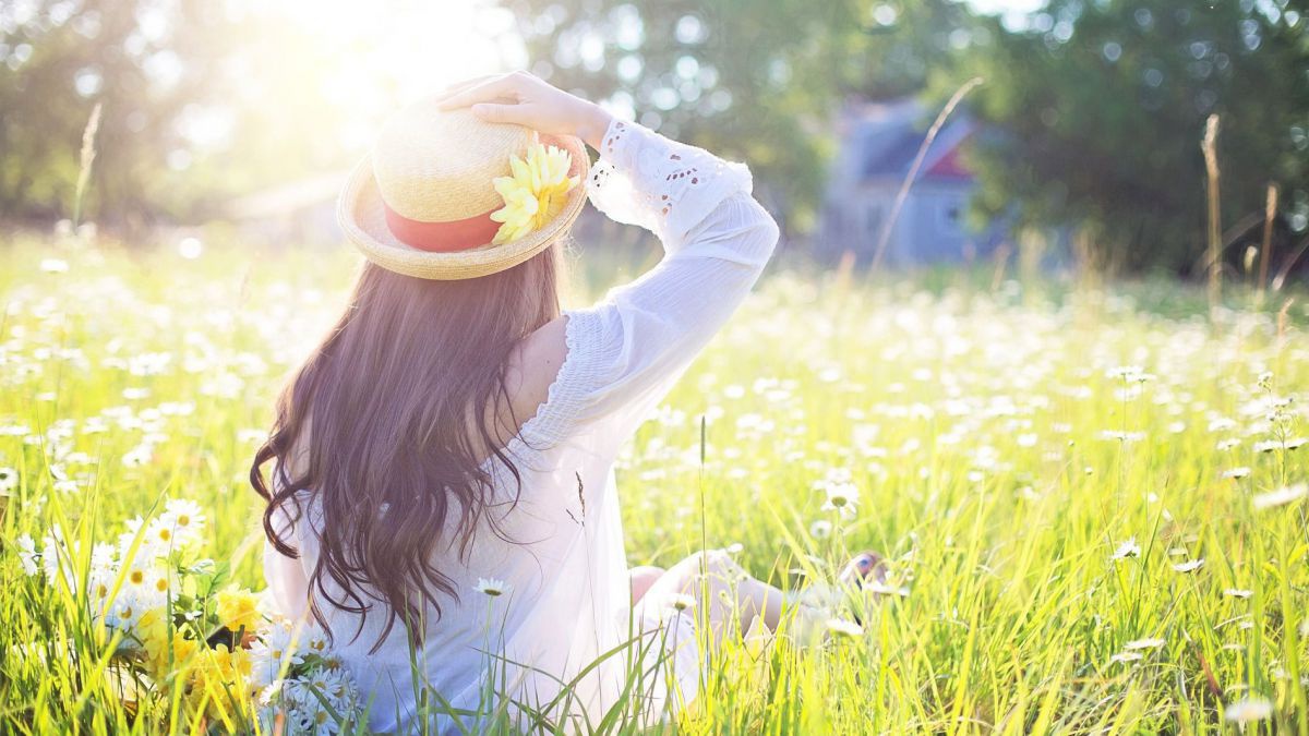 Frau mit Sonnenhut sitzt in der Wiese.