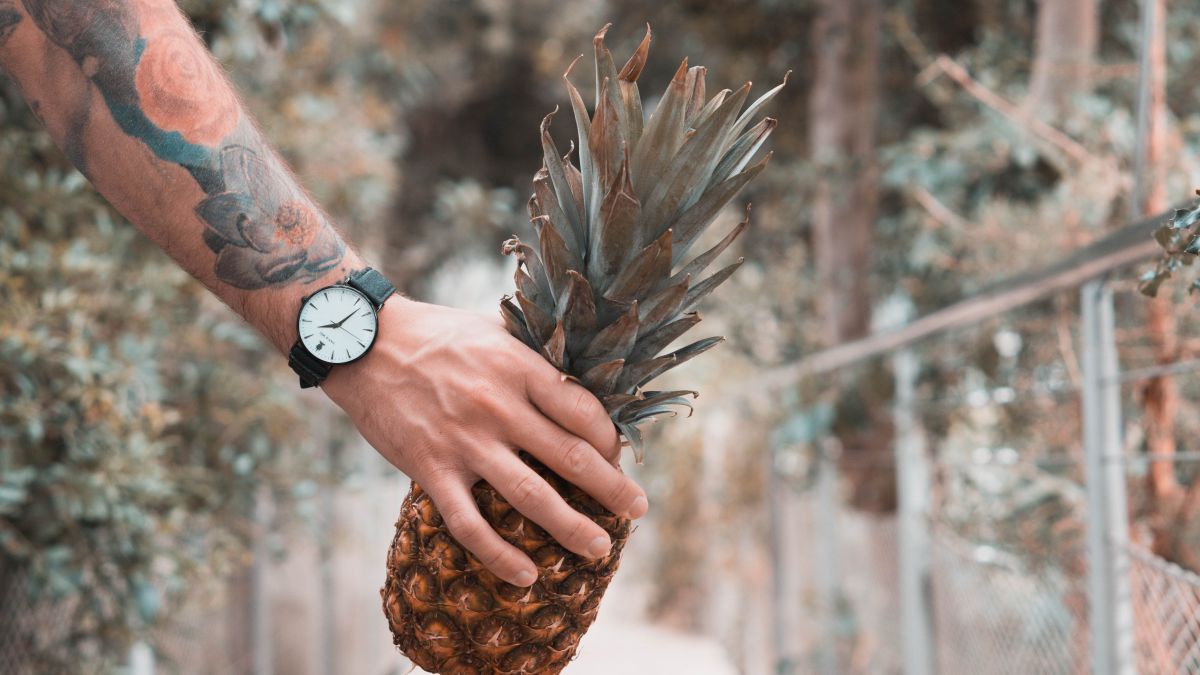 Arm mit Uhr am Handgelenk hält Ananas. 
