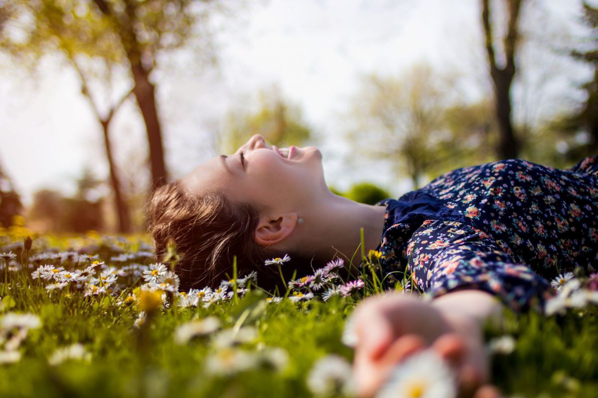 Frau liegt lächelnd in einer Blumenwiese.