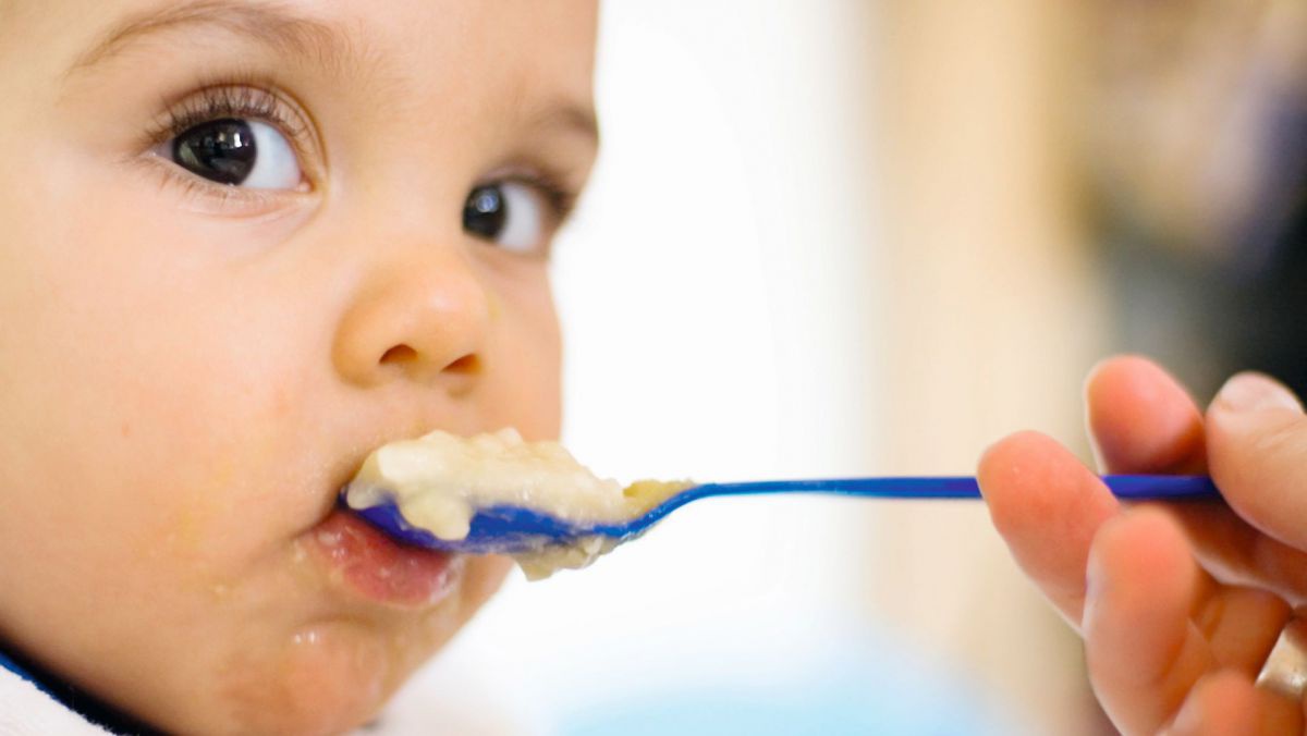 Baby mit Löffel voll Brei vor dem Mund.
