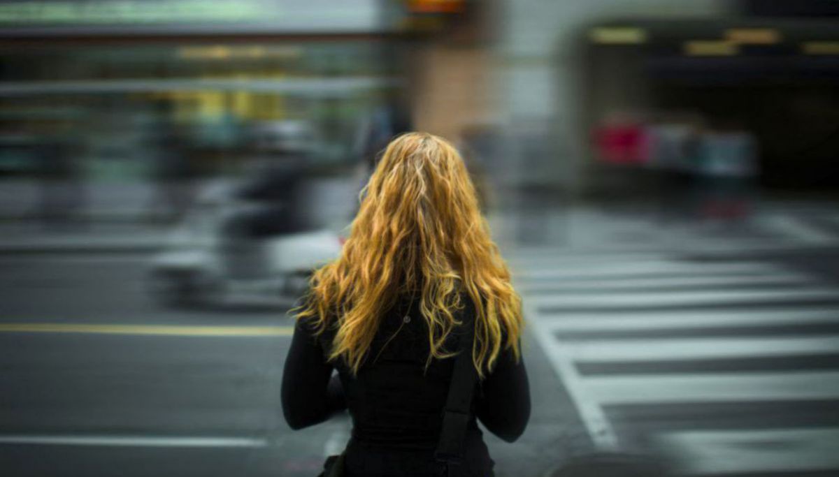 Frau mit langen Haaren steht an befahrenem Straßenübergang