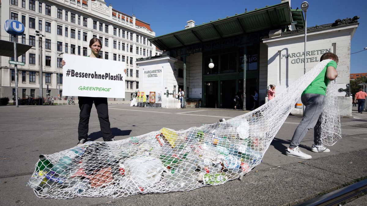 Eine Person zieht ein Netz voller Plastikmüll vor der U-Bahn Station Margaretengürtel hinter sich her, während eine andere ein Schild mit #besserohnePlastik hochhält