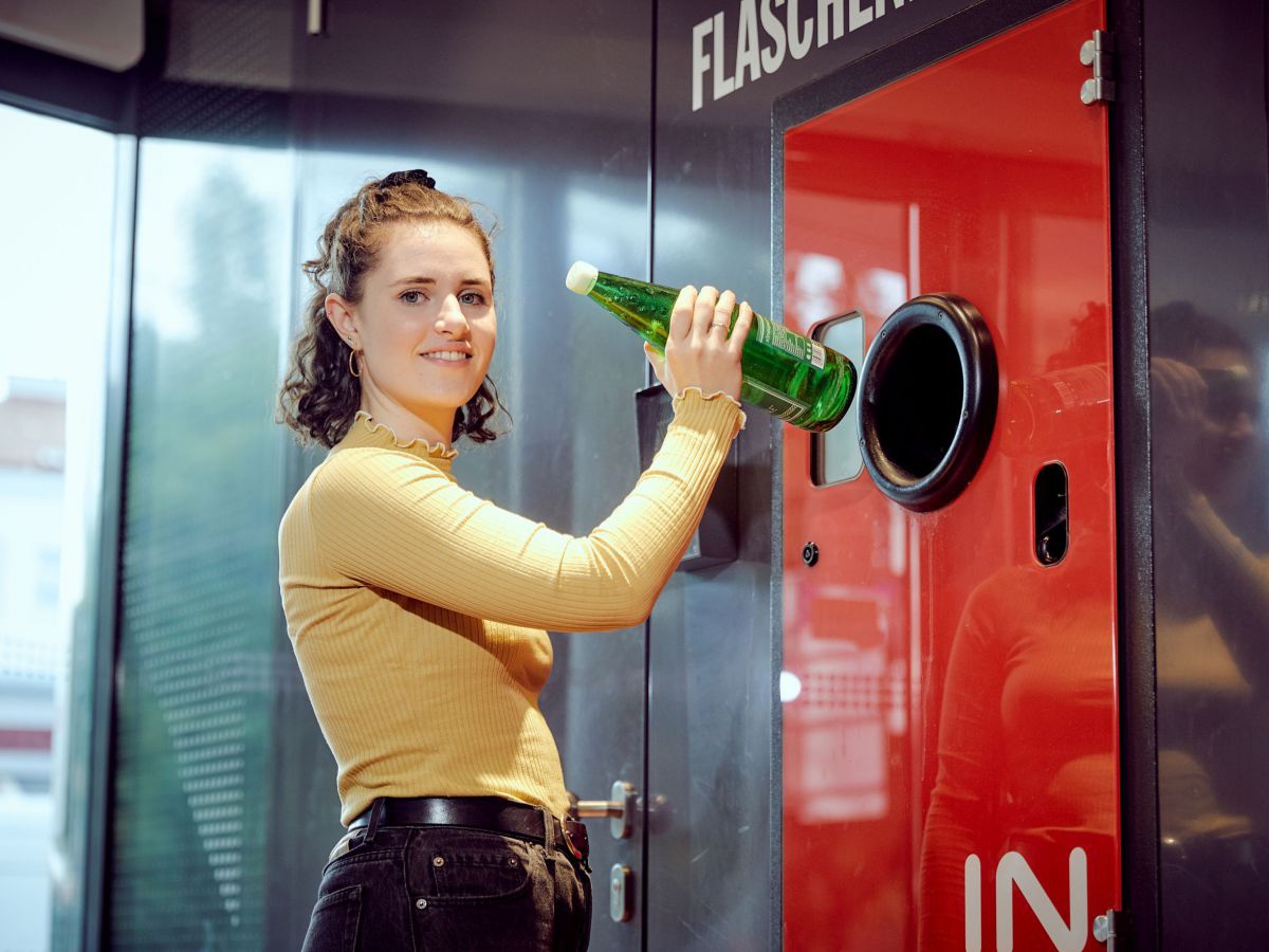 Eine junge Frau wirft eine Glasflasche in einen Leergutrücknahmeautomaten.