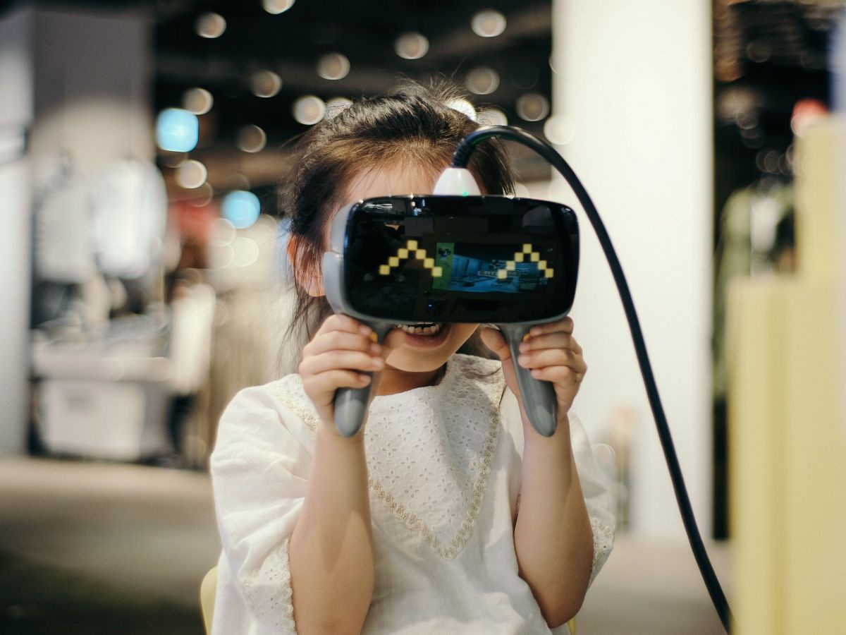 Ein Mädchen hält sich lachend eine VR-Brille vors Gesicht.