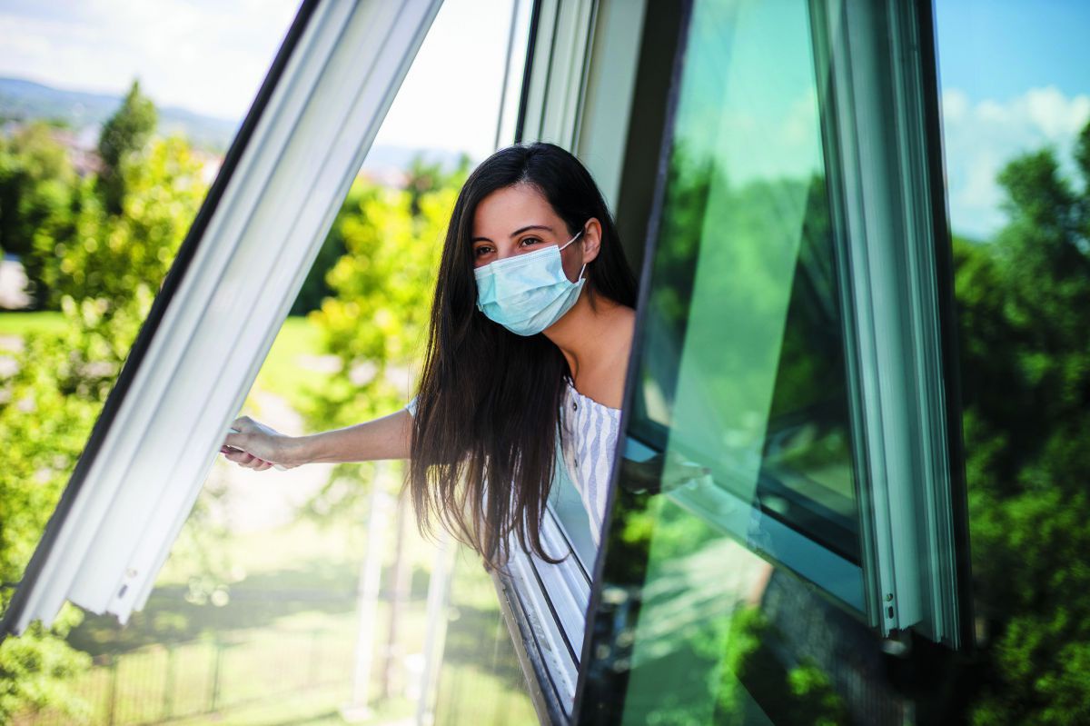 Eine Frau mit Mund-Nasenschutz öffnet ein Fenster.