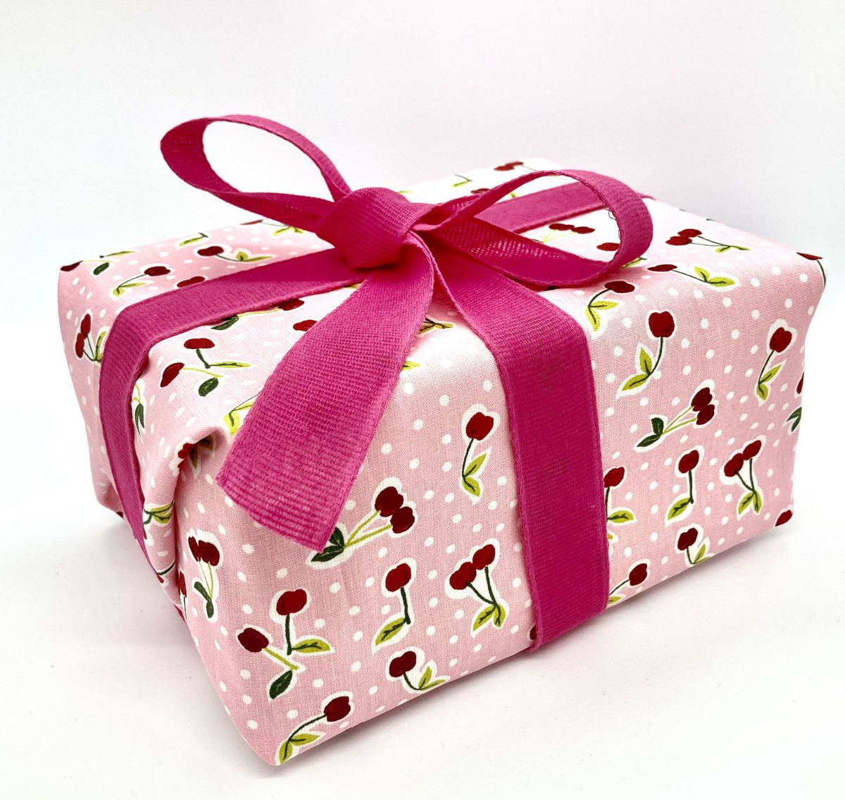 Ein Paket mit pinkter Schleife und rosa Geschenkstoff, der mit Kirschen und weißen Punkten bedruckt ist.