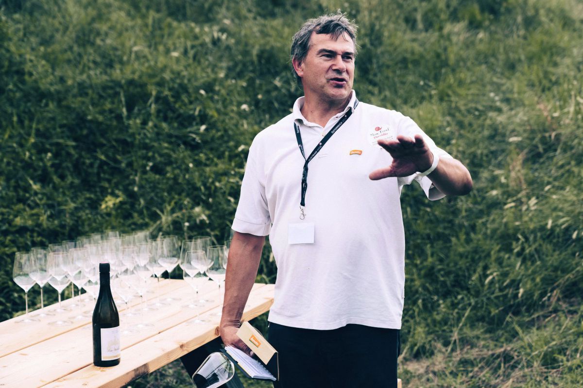 Hans Czerny erklärt erwas. Er steht im Freien, neben ihm ein Tisch mir Weingläsern und Flasche.