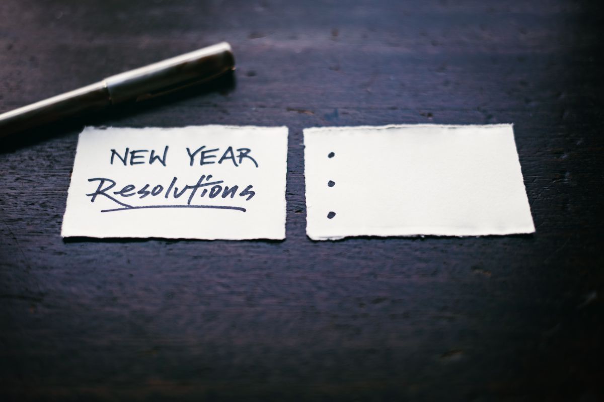 Zwei Zettel auf dunklem Untergrund. Auf einem steht New Year Resolutions, auf dem anderen sind drei Aufzählungspunkte. Daneben liegt ein Füller.