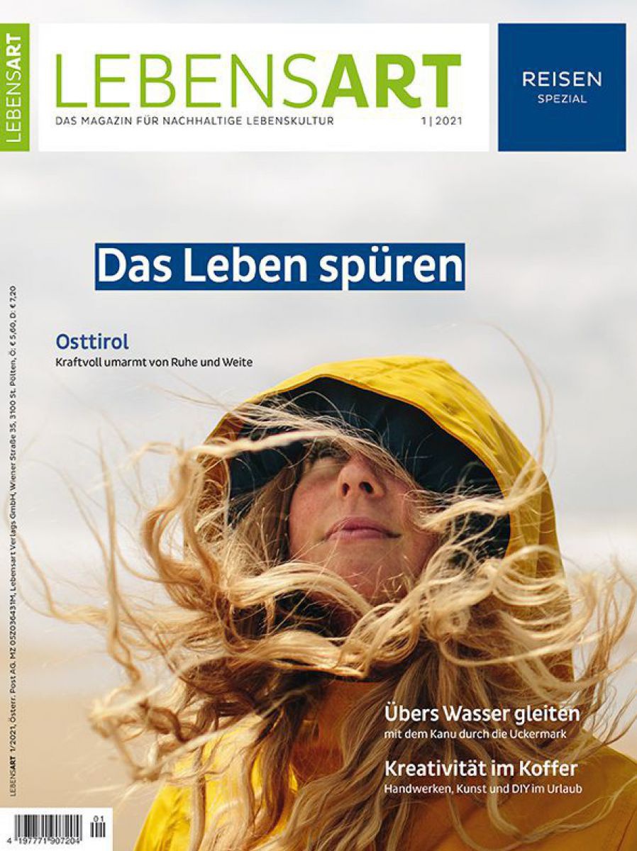 Eine Frau im gelben Regenmantel blickt zum Himmel auf. Ihr Gesicht ist umrahmt von der Kapuze und ihren langen blonden Haaren mit denen der Wind spielt.
