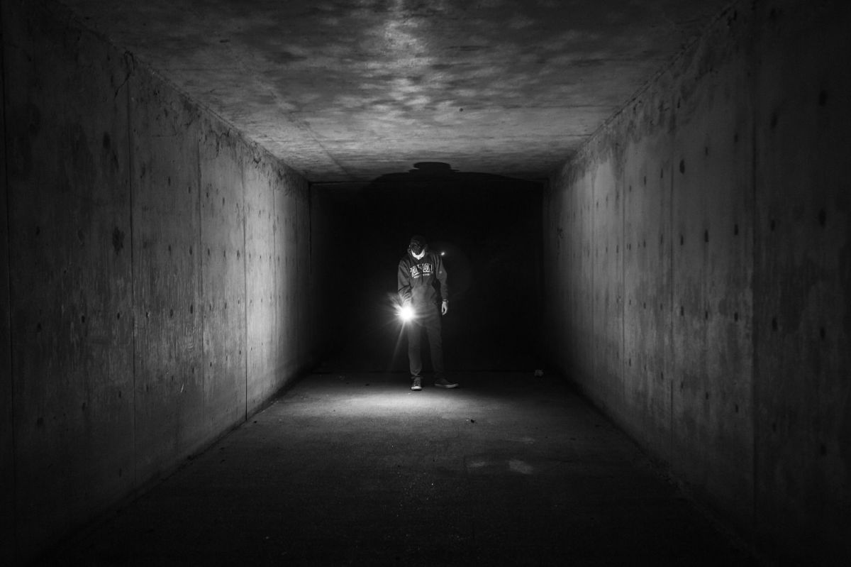 Eine Person geht in einem dunklen Schacht mit einer Taschenlampe.