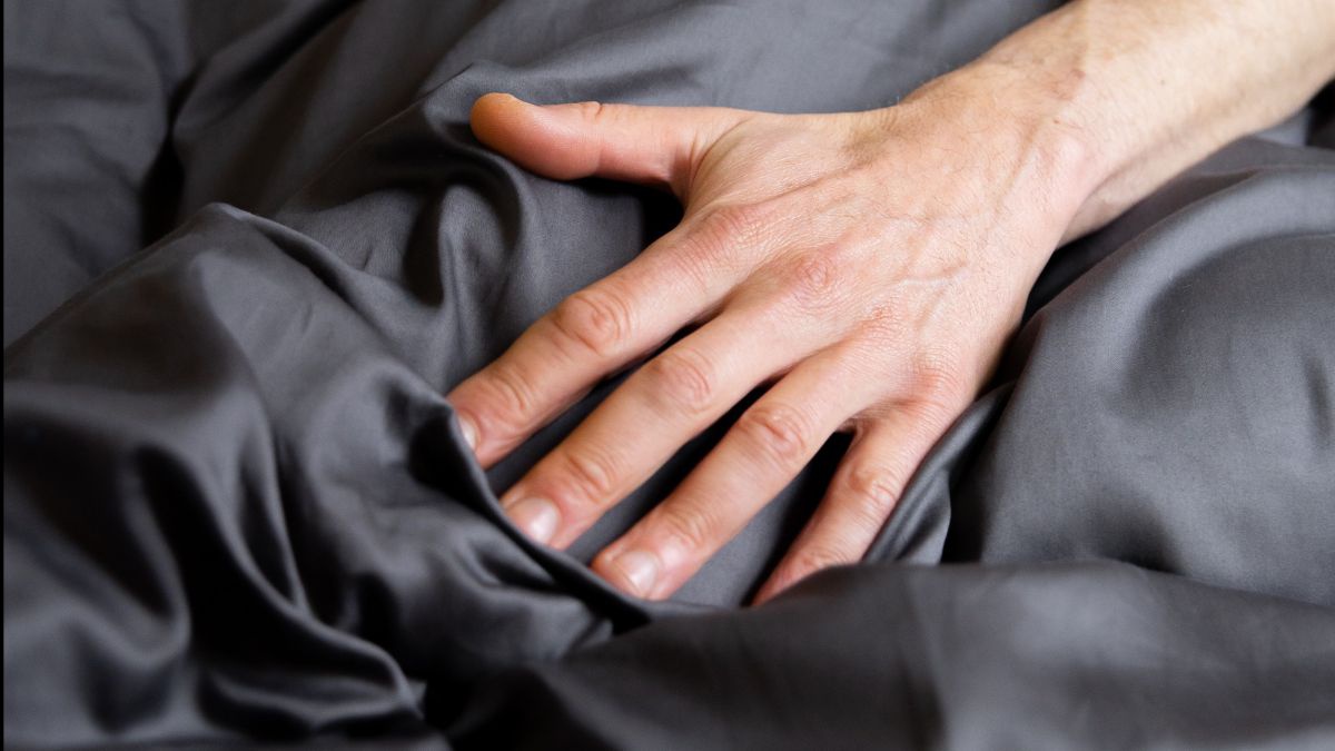 Eine Hand streicht sanft über dunkelgraue Bettwäsche die leicht glänzt.
