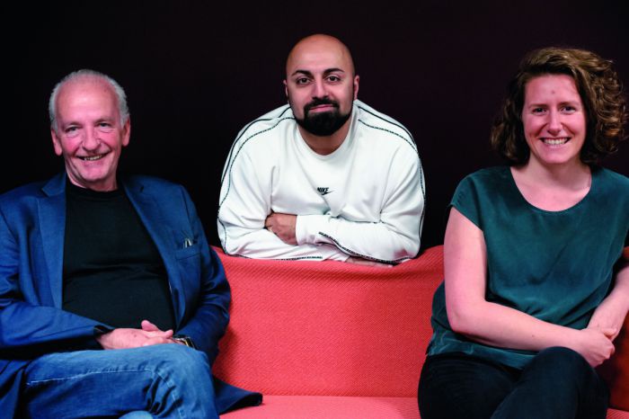 Das Sieger*innenfoto der nachhaltigen Gestalter*innen 2020: Sepp Eisenriegler und Katharina Rogenhofer sitzen auf einem roten Sofa, mittig zwischen ihnen stützt sich Ali Mahlodji auf die Sofalehne. Alle drei lächeln in die Kamera.