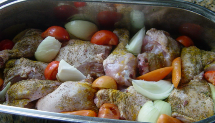 Eine Ofenform mit gewürzten Hühnerteilen und Gemüse.