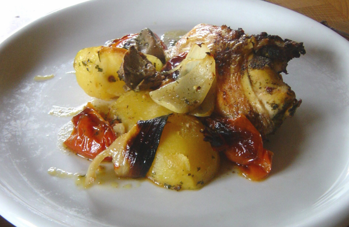 Eine bute Mischung aus Kartoffel, Zwiebel, Tomate und Huhn, frisch aus dem Ofen auf einem weißen Teller.