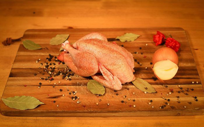 Ein gewürztes Hühnchen appetitlich auf einem Brett mit aufgeschnittener Zwiebel und Gewürzen angerichtet.