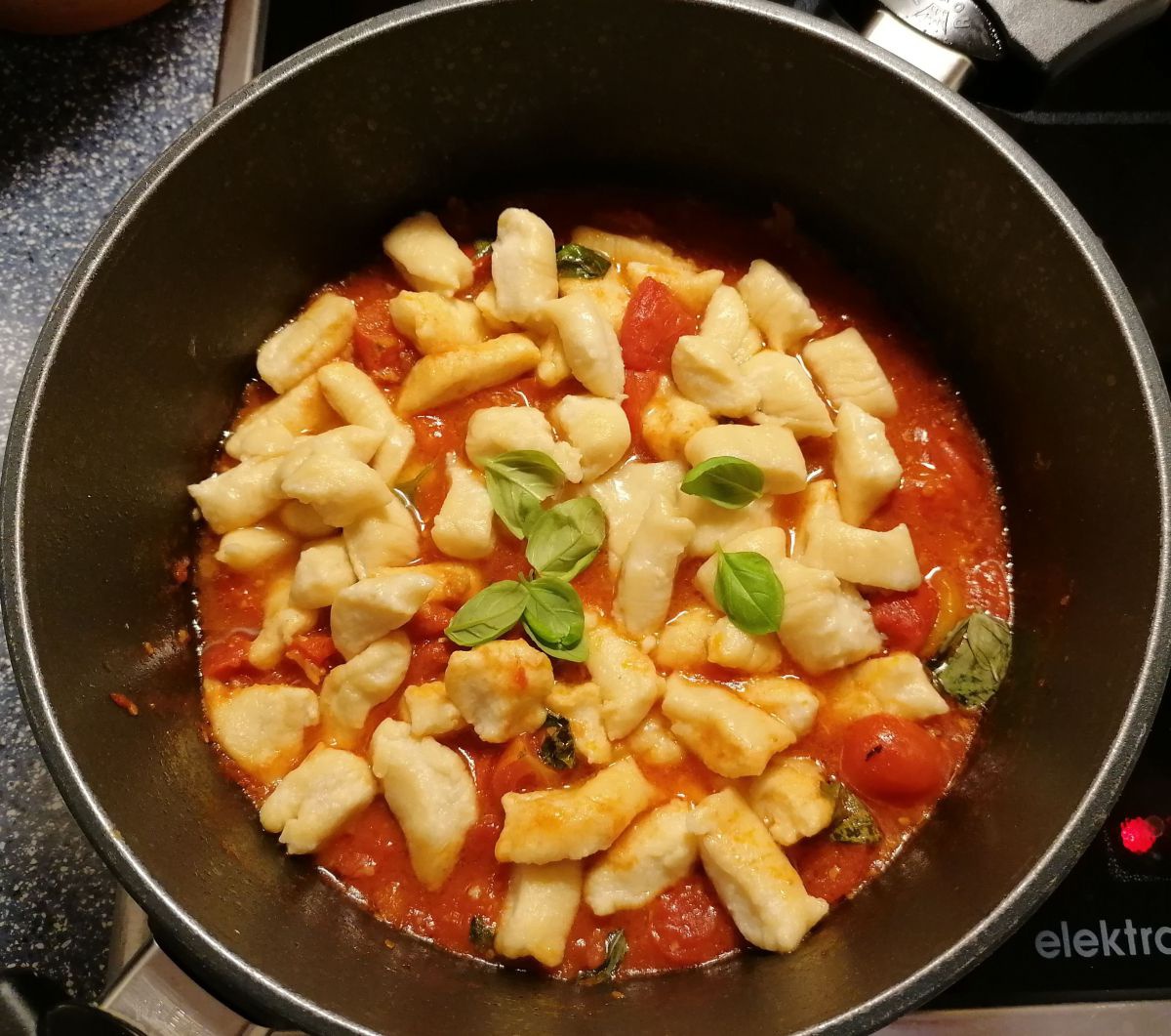 Eine Pfanne mit selbstgemachten Gnocchi in einer Tomatensauce mit einigen Blättern Basilikum.
