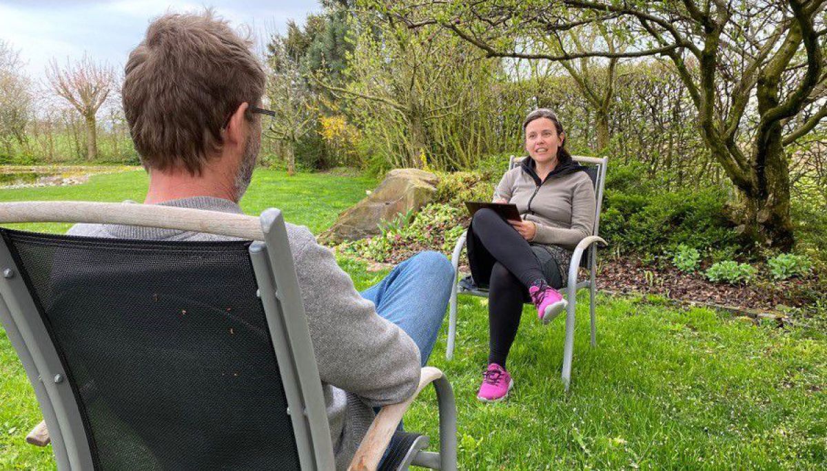 In einem Park sitzen sich zwei Menschen mit etwas Abstand gegenüber auf zwei Sesseln und sprechen miteinander.