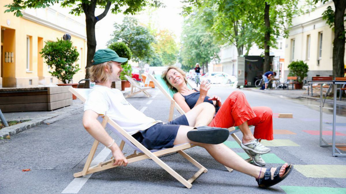 Auf einer Straße sitzen zwei Personen in Liegestühlen.