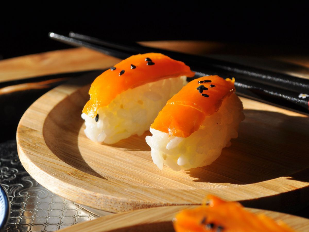 Sushi mit Karottenlachs und schwarzem Sesam vor dunklem Hintergrund. 