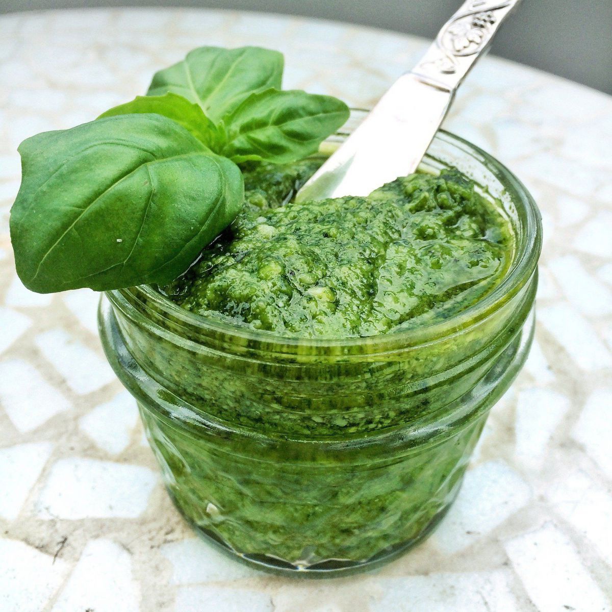 Ein Glas Basilikumpesto, mit frischem Baslikum garniert.