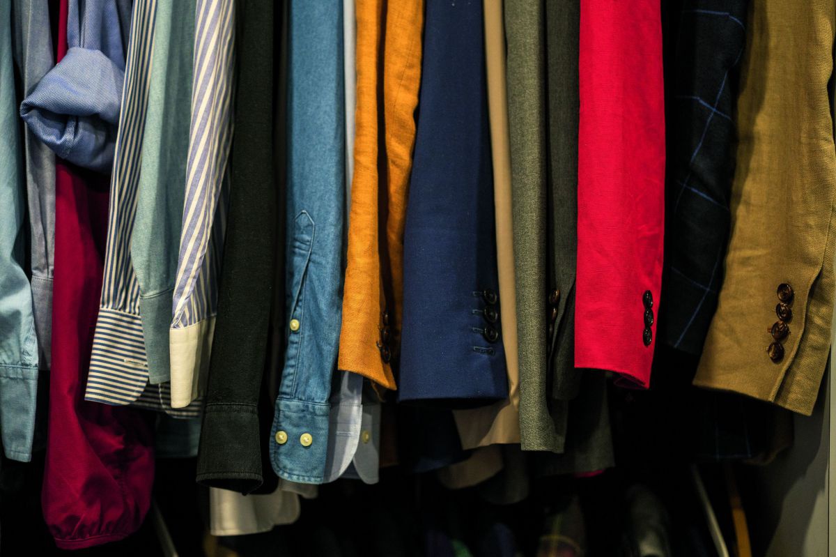 Kleidung im Kleiderschrank. Man sieht die Ärmel von Hemden und Blazern die auf Bügeln hängen.