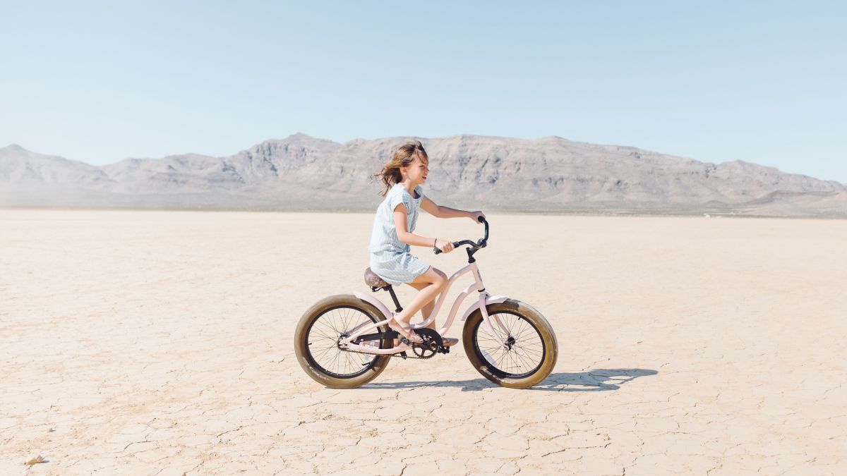 Ein Mädchen fährt in der Wüste Fahrrad. Der Boden ist trocken und rissig.