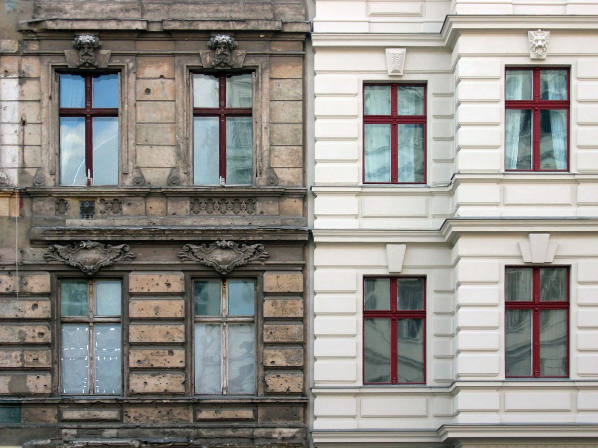 Die Fassade von zwei Häusern in Wien. Eine ist frisch gestrichen beige, die andere vergilbt und verschmutzt.