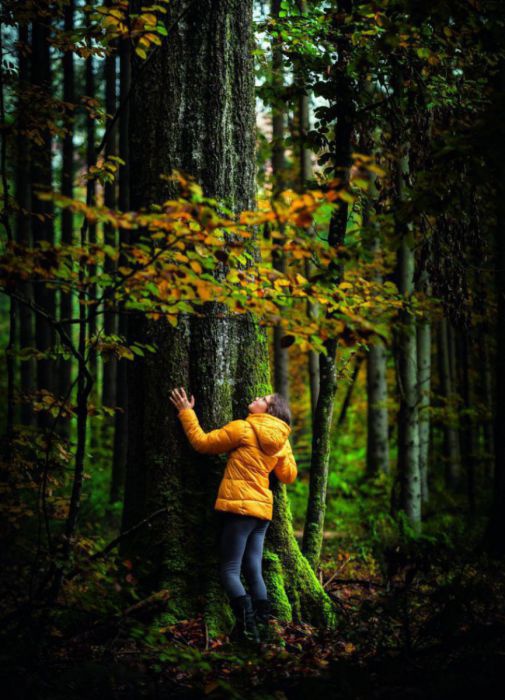 Eine Jugendliche in gelber Daunenjacke umarmt einen Baum.