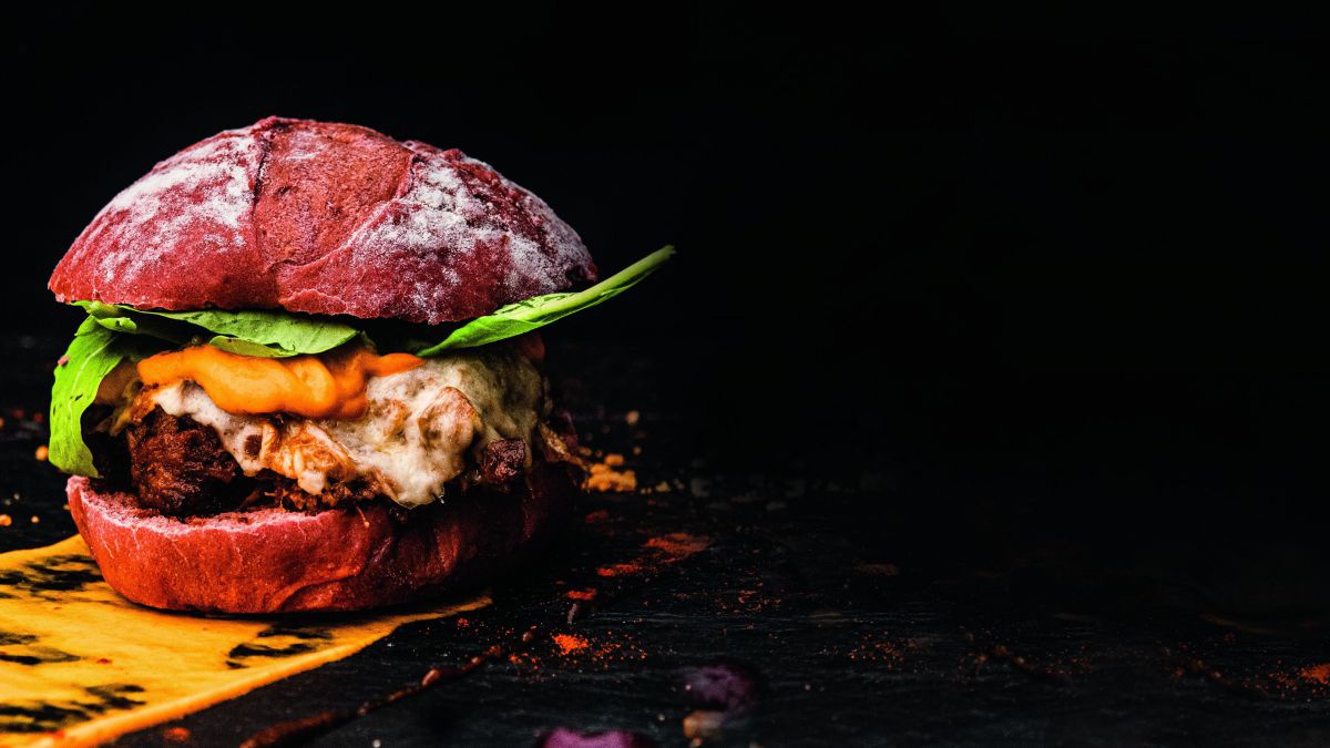 Ein schön angerichteter Burger im Vollkornbun vor schwarzem Hintergrund.