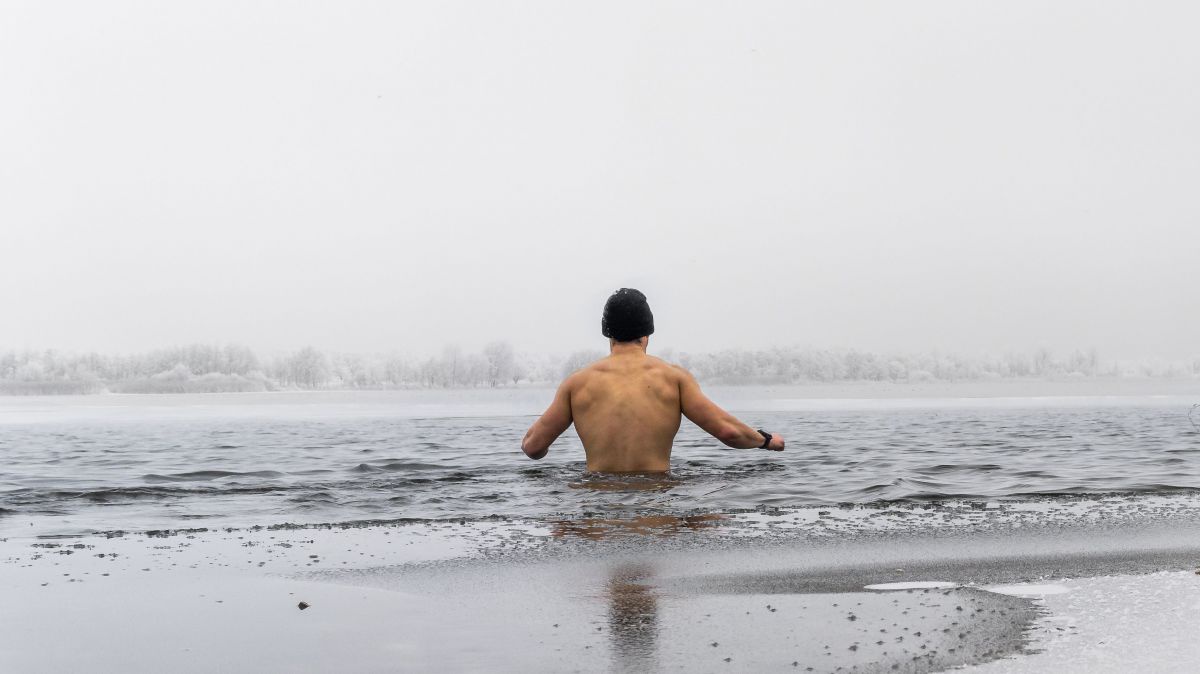 Ein Mann geht vom Ufer ins Wasser. Rundherum liegt Schnee.