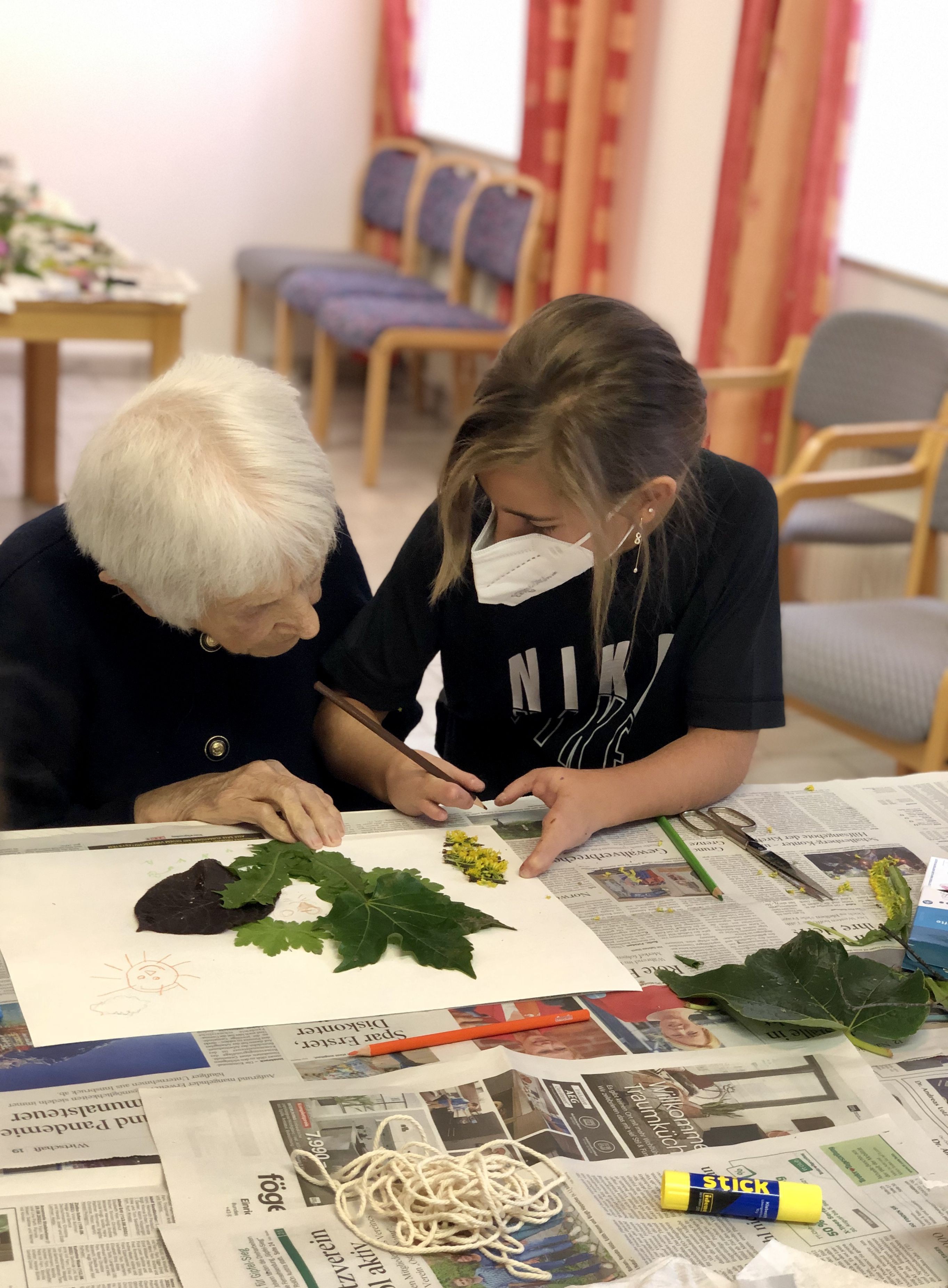 Eine alte Frau und eine Jugendliche legen Blätter auf einem Blatt Papier auf.