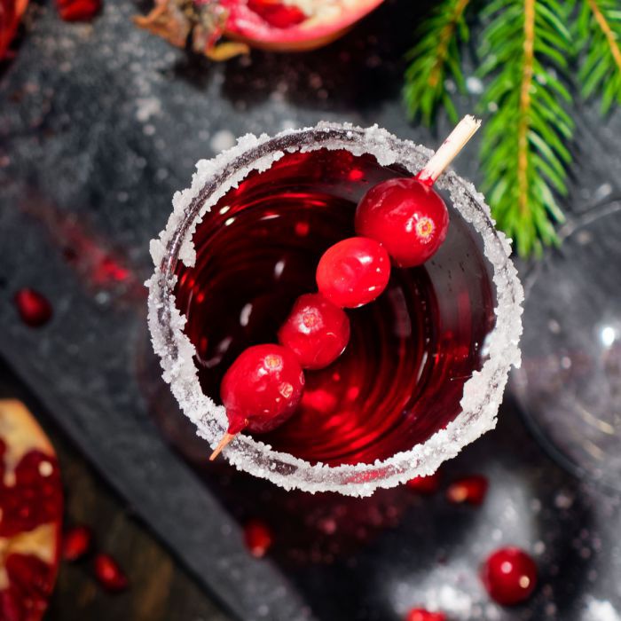 Ein roter Cocktail von oben. Das Glas hat einen Zuckerrand, auf einem Zahnstocher stecken vier Cranberries.