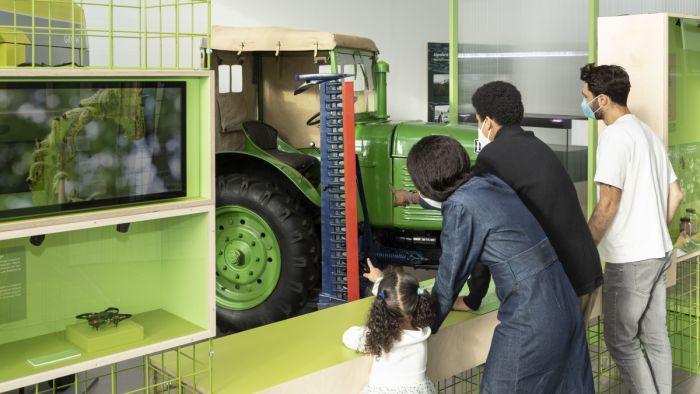 Im Ausstellungsraum steht ein grüner Traktor, mehrere Schaukästen und Videoscreens.