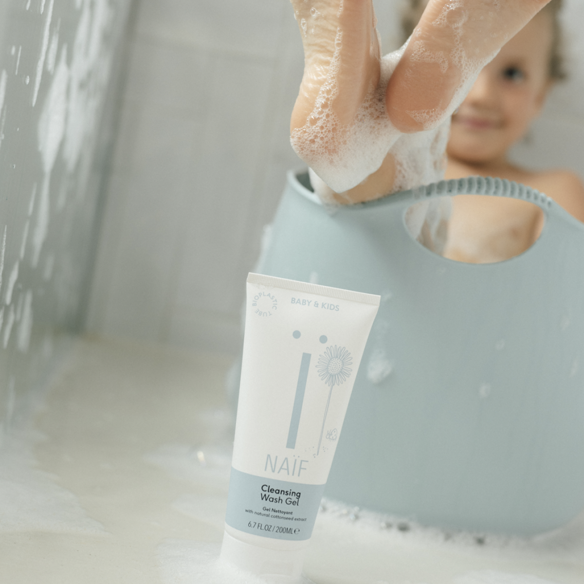 Ein Kind sitzt in einer Wanne und streckt seine Füße heraus. Es lächelt an den Füßen ist Badeschaum.