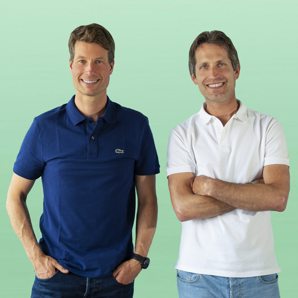 Die beiden Männer stehen vor einem Minzgrünen Hintergrund. Sie lächeln in die Kamera.