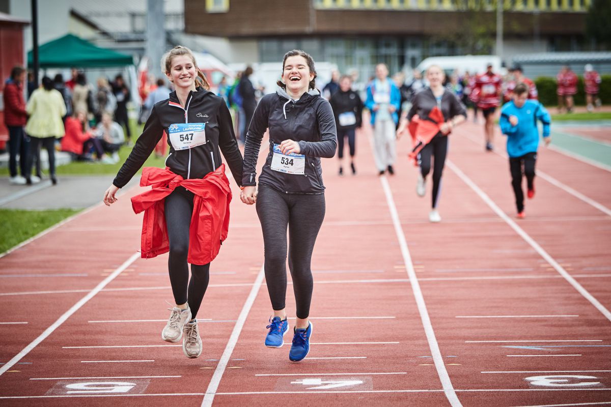 Zwei junge Frauen laufen auf einer Laufbahn. Sie halten sich an den Händen.