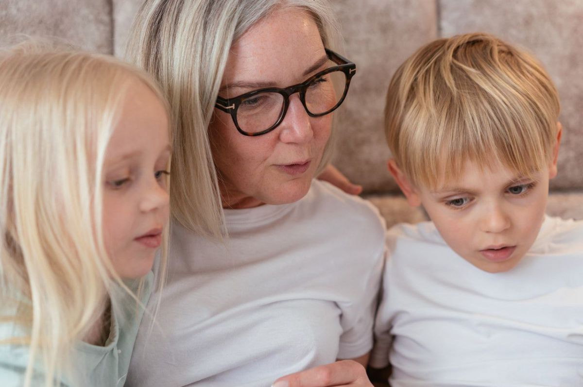 Eine Frau mit langen blonden Haaren spricht, zwei Kinder hören konzentriert zu.