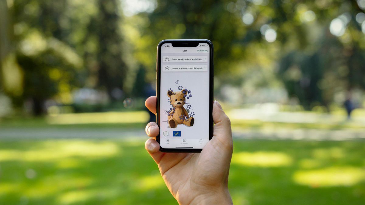 Eine Hand hält ein Handy hoch auf dessen Bildschirm ein Teddybär angezeigt wird. 